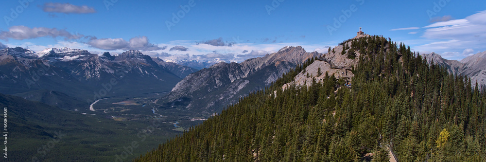 View of Sulphur Mountain peak with wooden boardwalk between trees in Banff National Park, Alberta, Canada with panorama of the rugged Rocky Mountains.