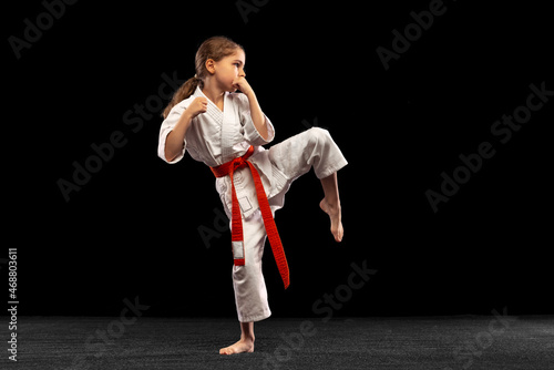 Karate, taekwondo girl with yellow belt isolated on dark background in neon light. Concept of sport, education, skills photo