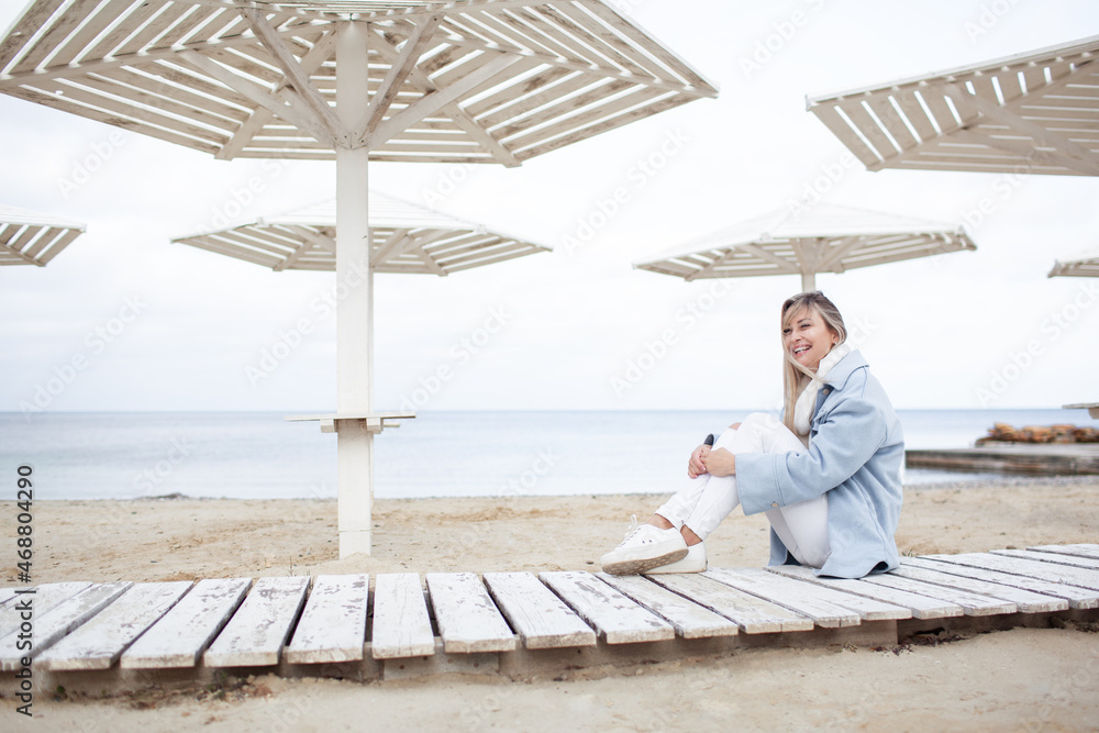 Beautiful woman dressed woolen blue jacket, white scarf and trousers walking in the beach, reston and enjoy the time is in with you, against the shore of the beach at background sea and sky