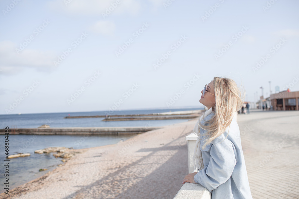 Beautiful woman dressed woolen blue jacket, white scarf and trousers walking in the beach, reston and enjoy the time is in with you, against the shore of the beach at background sea and sky Beautiful woman dressed woolen blue jacket, white scarf and trousers walking in the beach, reston and enjoy the time is in with you, against the shore of the beach at background sea and sky