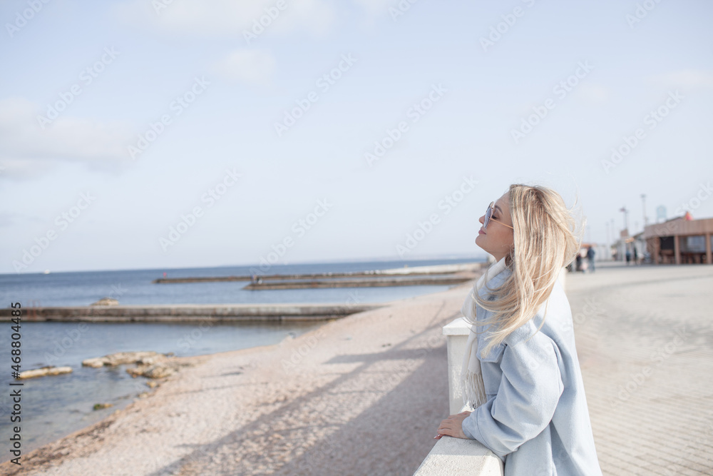 Beautiful woman dressed woolen blue jacket, white scarf and trousers walking in the beach, reston and enjoy the time is in with you, against the shore of the beach at background sea and sky