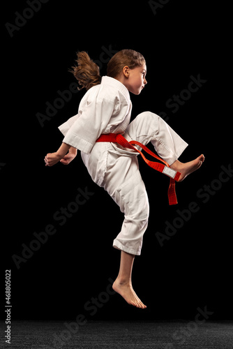 Karate, taekwondo girl with yellow belt isolated on dark background in neon light. Concept of sport, education, skills