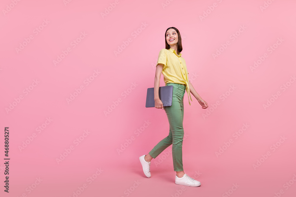 Full size profile side photo of young girl happy smile go curious look empty space hold laptop isolated over pink color background Full size profile side photo of young girl happy smile go curious look empty space hold laptop isolated over pink color background