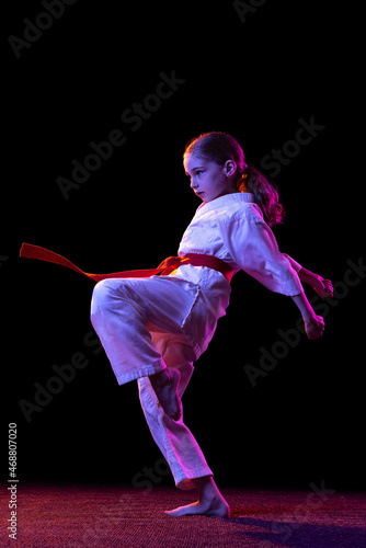 Karate, taekwondo girl with yellow belt isolated on dark background in neon light. Concept of sport, education, skills © master1305