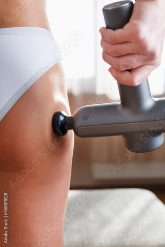 Self-massage of the female buttock with a percussion massage gun at home.
