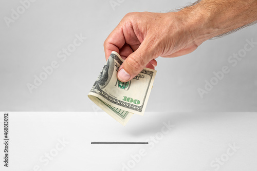 Photography Male hand putting 100 U.S. dollars money into donation box