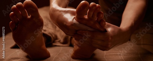 The masseur gives a foot massage to the client. Close-up of hands covered with oil. Subdued lights in the spa. Horizontal banner for website and social networks