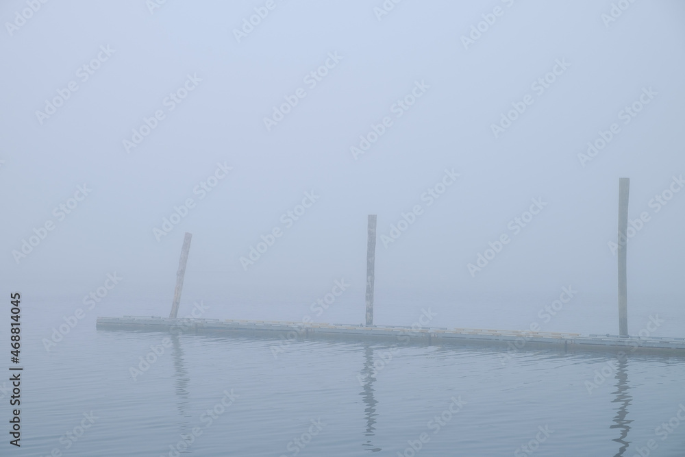 A small wooden boat dock enveloped in thick fog reflected in the calm waters of Rockland Bay
