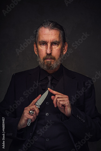 man in black suit checks the sharpness of his knife