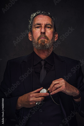 man in black suit winding a pocket watch