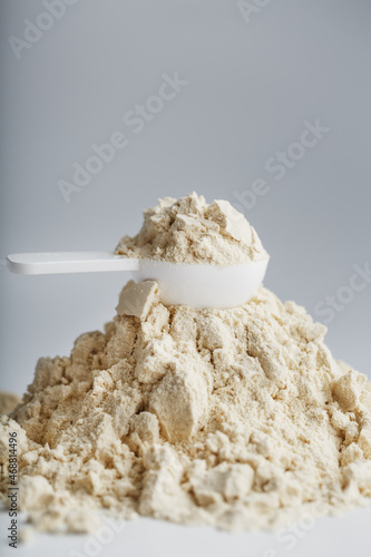 A pile of protein powder with a measuring spoon on a white background.