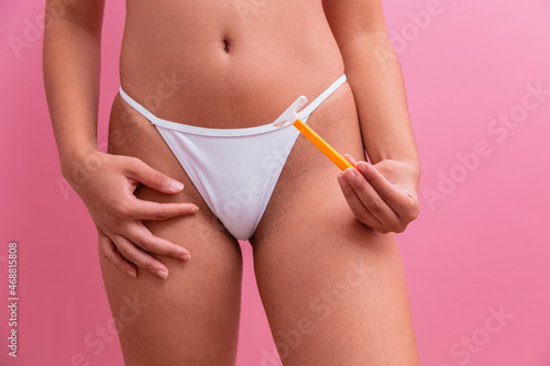 Closeup of a girl in white panties holding a yellow razor blade in her hands on a pink background. photo