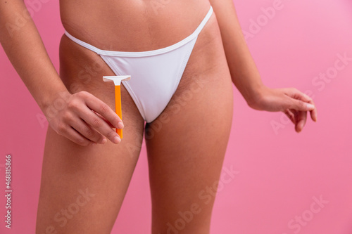 Closeup of a girl in white panties holding a yellow razor blade in her hands on a pink background. photo