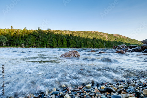 Granite boulders and smaller broken up and smoothed rocks line the shoreline of Jordan Pond in Maine during a windy and rough water day