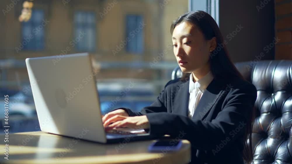 young female freelancer or student working online or studying remotely in a cafe. Asian business woman in suit uses laptop at workplace in coworking young female freelancer or student working online or studying remotely in a cafe. Asian business woman in suit uses laptop at workplace in coworking