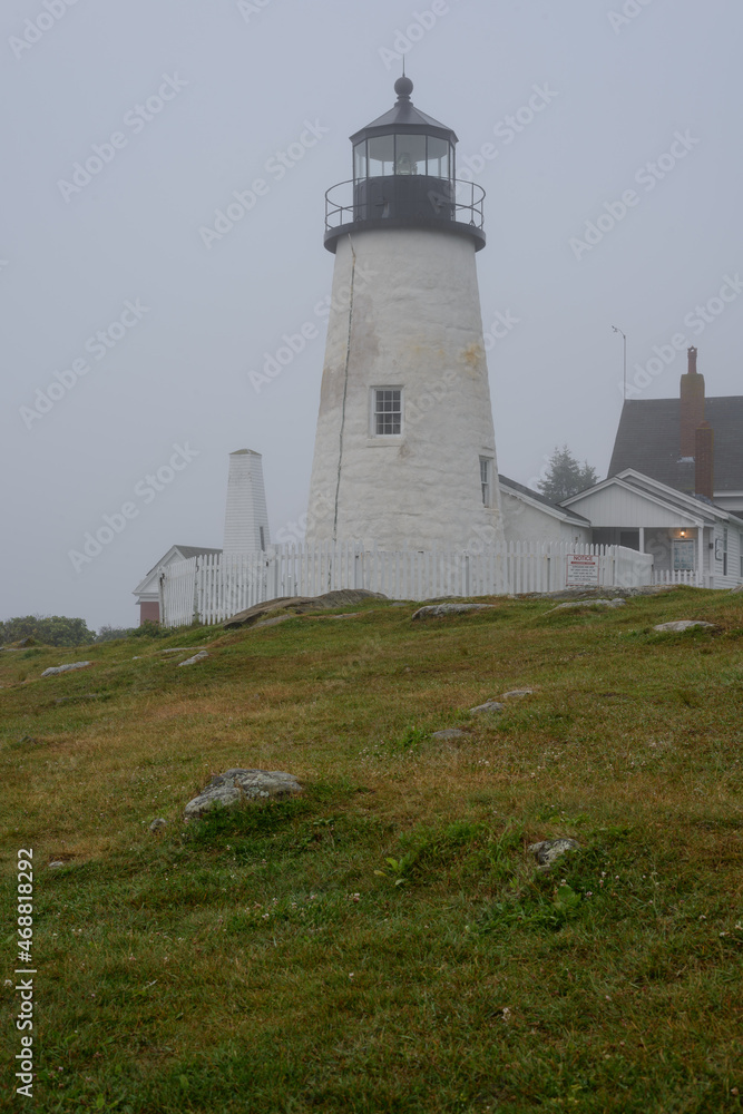 The old Pemaquid Lighthouse enveloped in heavy fog sits on the edge of the Atlantic Ocean on the Maine Coast early morning