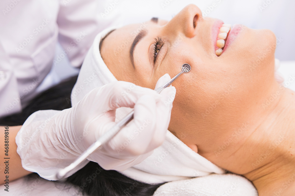 Cosmetician in protective gloves performs a cosmetic procedure on the patient's face using medical instrument tool for removal acne, comedones, impurities from the face. Cosmetician in protective gloves performs a cosmetic procedure on the patient's face using medical instrument tool for removal acne, comedones, impurities from the face.