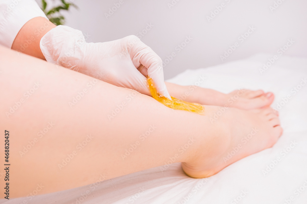 Naklejka premium Professional cosmetologist in beauty salon making waxing, an depilation procedure for removing hair from the leg using sugaring paste on white background