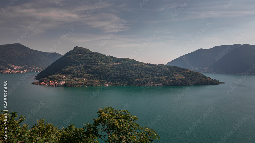 Island Monte Isola in Lake Iseo from above, mountains in the background, during blue sky day, Italy.