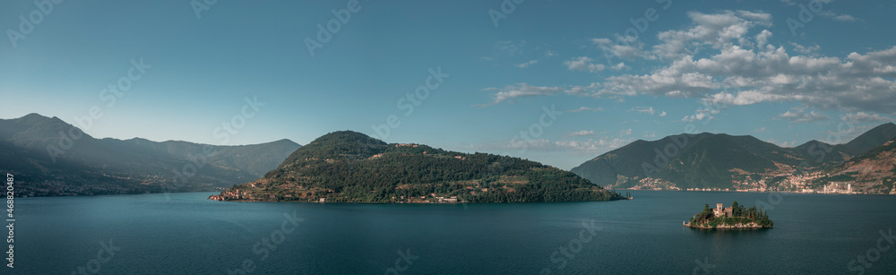 Mountain panorama at Lake Iseo with island Isola di Loreto and Monte Isola from above during afternoon, blue sky, Italy.