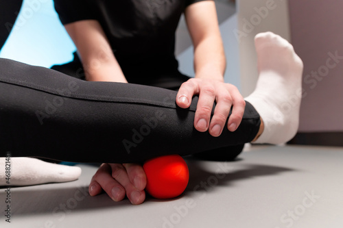 Close-up young male massage therapist teaches a client Caucasian woman myofascial self-massage using a massage ball indoors. Myofasceal release