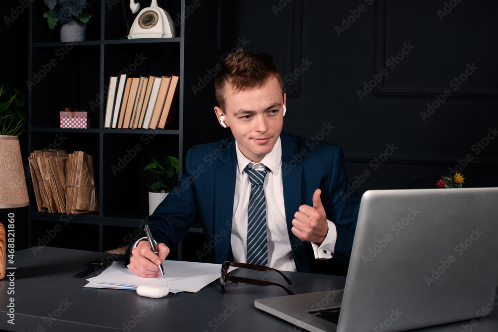 A young businessman is holding an online conference through a laptop. The man works remotely. A young businessman is holding an online conference through a laptop. The man works remotely.