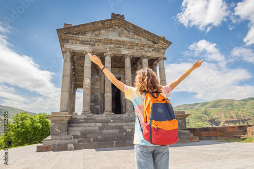 A happy woman traveler or student with backpack at the Garni Temple in Armenia - an ancient monument listed in UNESCO © EdNurg