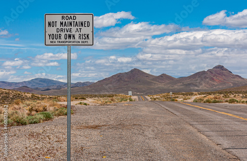 Tonopah, Nevada, US - May 16, 2011: Sign on not maintained road leaving downtown under blue cloudscape with gray mountains in back. Some sparse green vegetation.