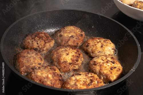 Cooking cutlets in a frying pan on an induction hob. White steam is hovering over hot cutlets in a frying pan