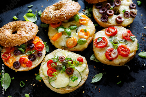 Grilled bagels with with mix vegetables, mozzarella cheese and herbs on a dark background, focus on the sandwich with zucchini slices, close up view.