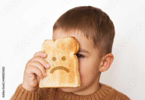 Children and gluten. Preschool boy with toasted bread, with sad emoji. Gluten intolerance by kids. photo