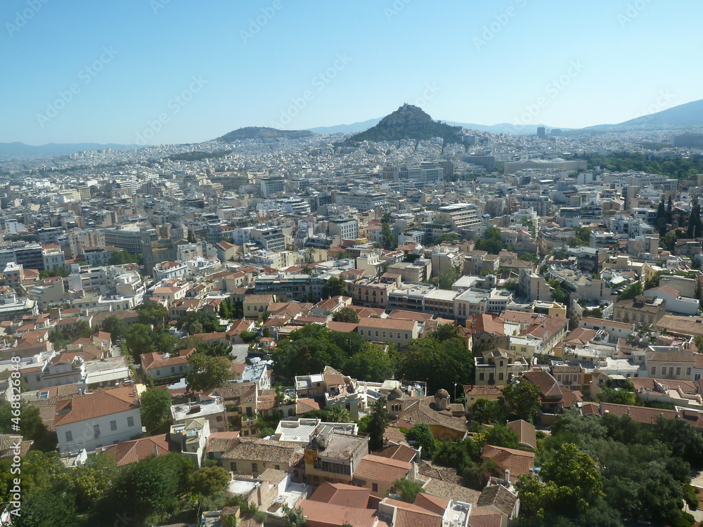 La célèbre ville d'Athènes, grande agglomération avec ses maisons blanches, et sa végétation torride, ainsi que ses monts tout autour, sous un beau jour