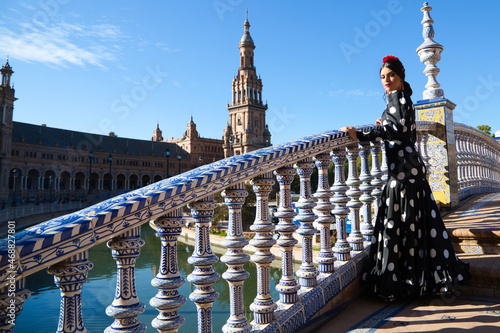Spanish, beautiful, brunette flamenco dancer with a typical flamenco dress in black with white polka dots. She is in the plaza spain in Seville. Flamenco concept cultural heritage of humanity.