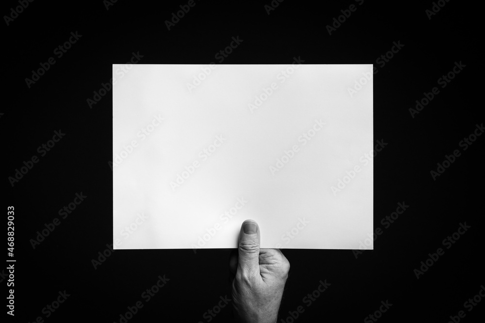 Hand holding blank sheet of paper against black background. Hand holding blank sheet of paper against black background.