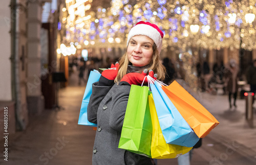 girl in a red santa claus hat with gifts in hands on the street of the city. Christmas mood
