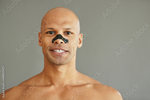 Happy African American man uses charcoal cleansing nose strips and looks at camera.