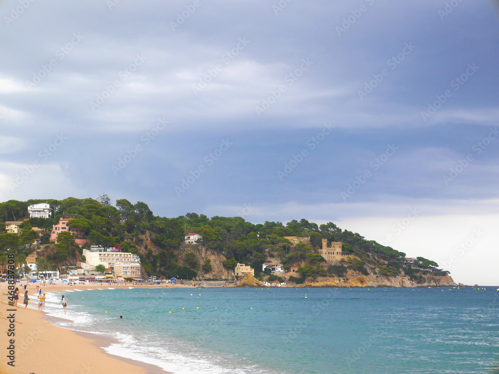 Colorful spanish coast, blue water and greenery. Sandy beach and clouds.