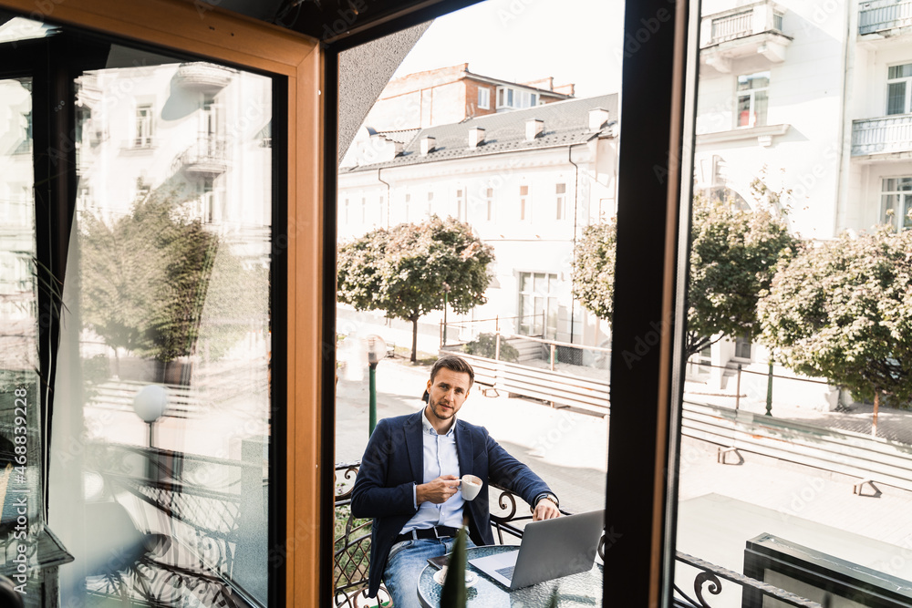 Handsome man with cup of coffee is working online using laptop in cafe. Remote work. Handsome man with cup of coffee is working online using laptop in cafe. Remote work.