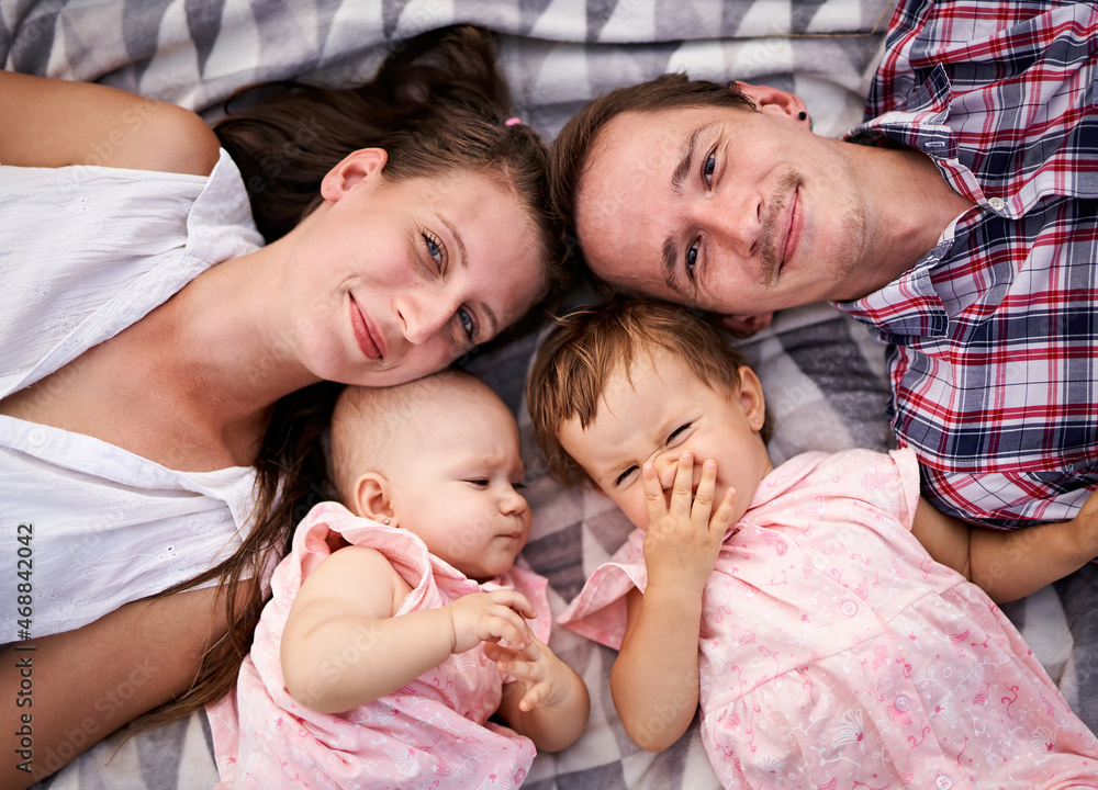 Happy family lies on a picnic blanket together - Young parents with a toddler and a baby daughter having fun - Bonding, love and care lifestyle concept from top view