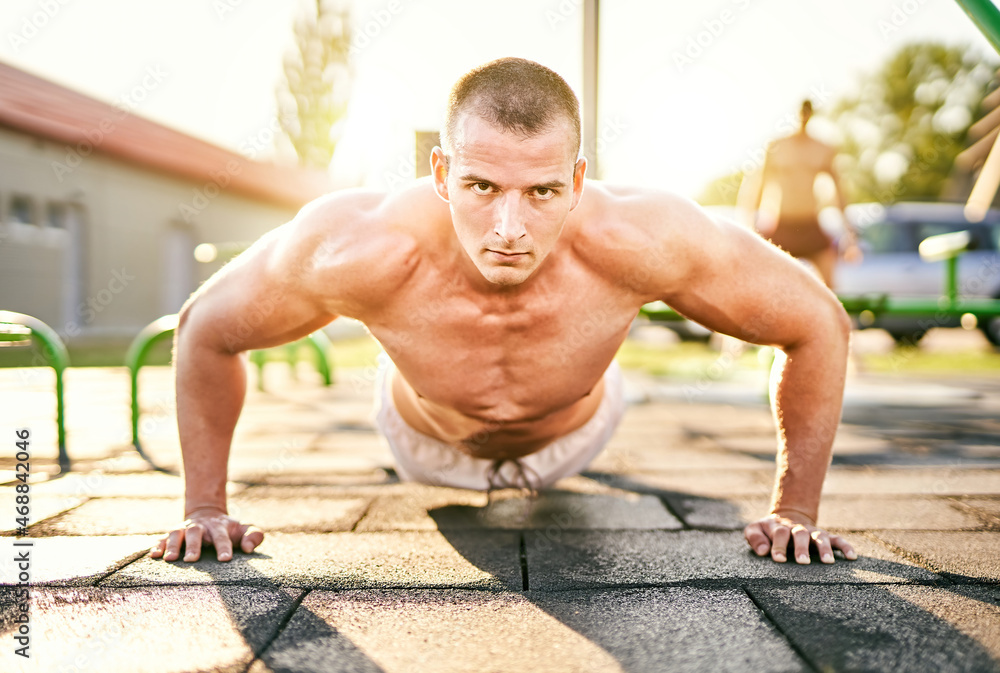 Millennial athletic muscular sportsman doing push ups in a fitness park outdoors - Focused male doing workout on the floor - Strength and bodybuilding concept