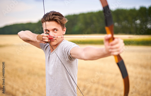 Young male sportsman targeting with traditional bow - Teenager archer practicing archery in nature - Outdoors sports and recreation concept with a millennial boy