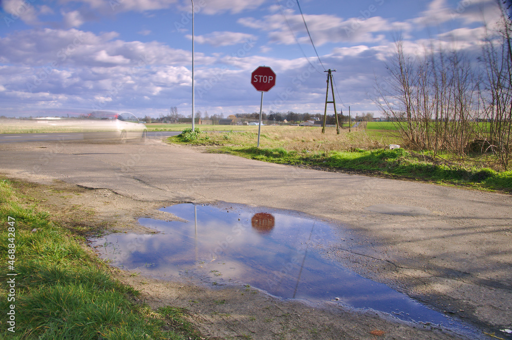 Znak STOP w odbiciu wody i rozmyty samochód z rozmytymi chmurami. - obrazy, fototapety, plakaty 