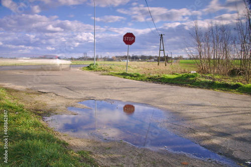 Znak STOP w odbiciu wody i rozmyty samochód z rozmytymi chmurami.