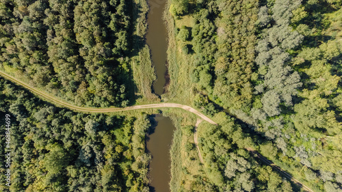Luftaufnahme von einem Waldweg in der Natur der über einen kleinen Fluss im Wald führt. 