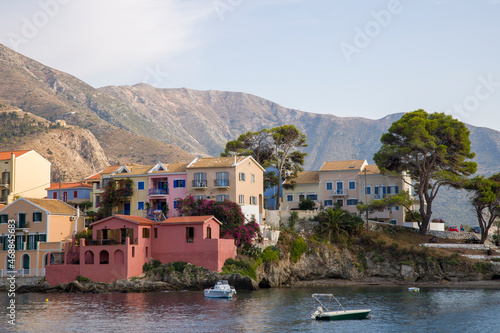 Panorama of the small town with bright multy-colored houses in the foot of the hills with mountains on horizon and small boats in the sea © Tetyana