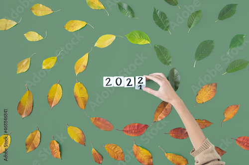 Red, green and yellow leaves forming a circle like movement of life or a cycle of year concept on green background in flat lay and 2022 cubes in middle hand switching year photo