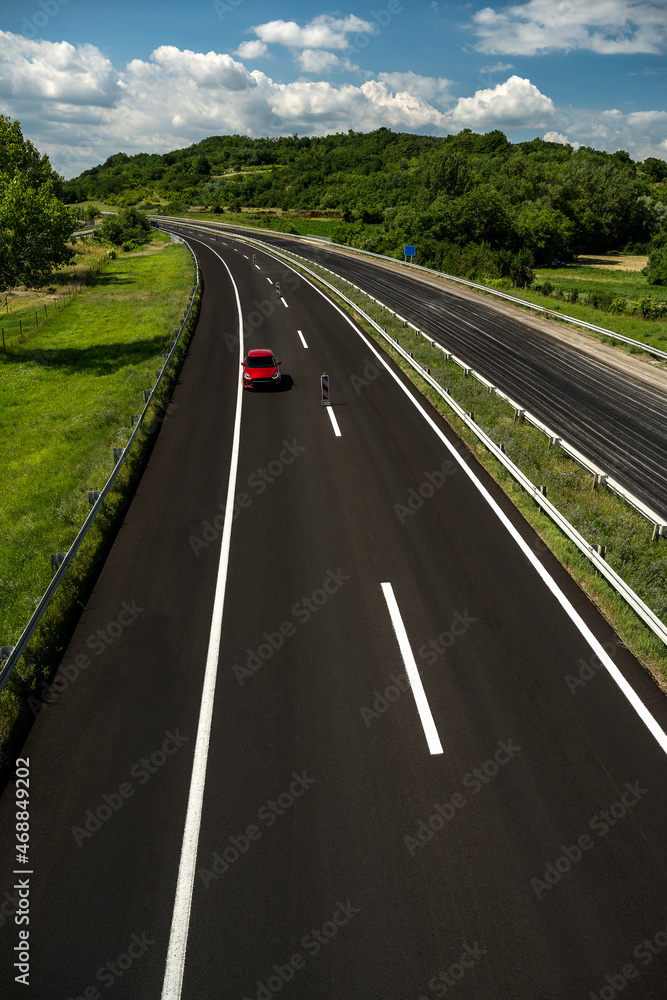 The red car is driving on the new highway. Red car driving along highway.