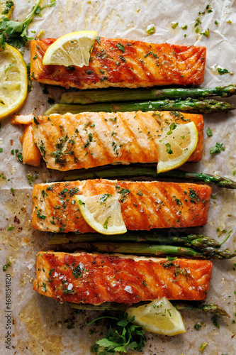 Grilled portions of salmon and green asparagus with lemon slices and herbs, top view