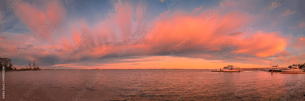 Panoramic arching pink cloudscape over the Plymouth Harbor. Twilight seascape at the marina in the Atlantic ocean.