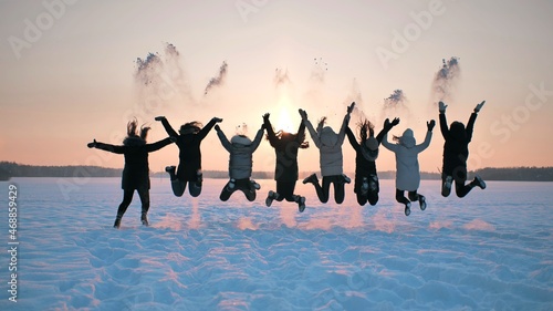 A group of girls friends are throwing snow up at sunset.